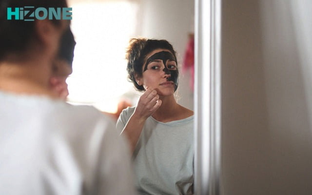 یک زن جلوی آینه در حال استفاده از ماسک زغالی
